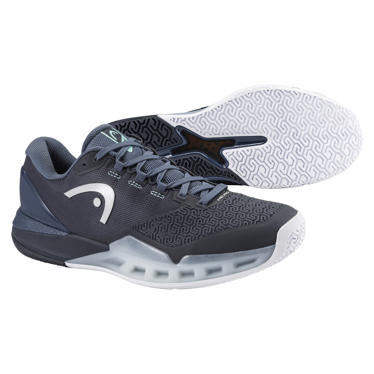 A studio product image of the HEAD Revolt Pro 5.0 men’s tennis shoe in a dark gray and navy colorway on a solid black background. One shoe is displayed in a clean side profile, highlighting the durable engineered mesh upper, reinforced toe cap with abrasion-resistant texture, supportive midfoot structure, and the sculpted midsole designed for stability and impact absorption. The second shoe is positioned behind it to clearly showcase the white non-marking outsole with an aggressive, multidirectional tread p