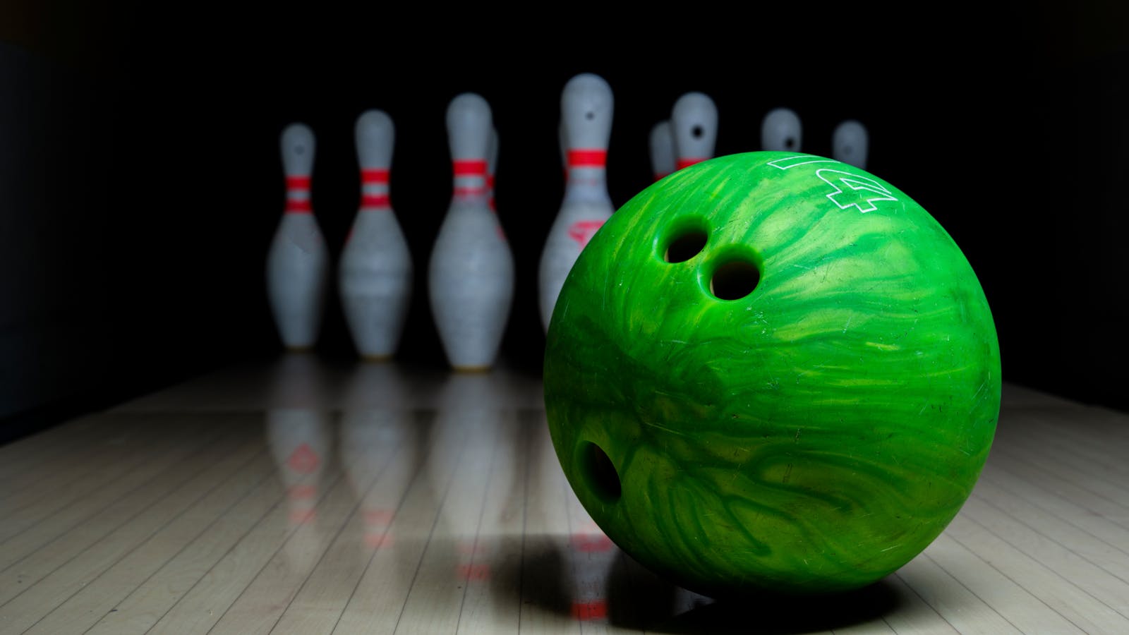 Green bowling ball rolling toward pins on polished lane