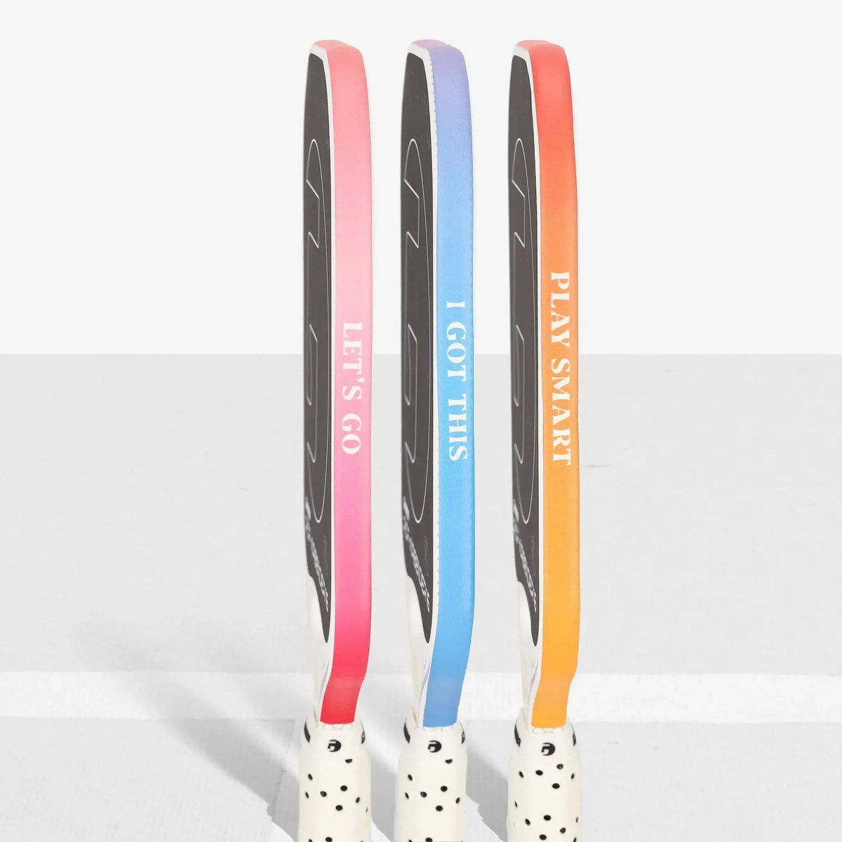Set of pickleball paddles shown from the side featuring edge guard tape with printed motivational phrases, designed to protect paddle edges from wear and impact.