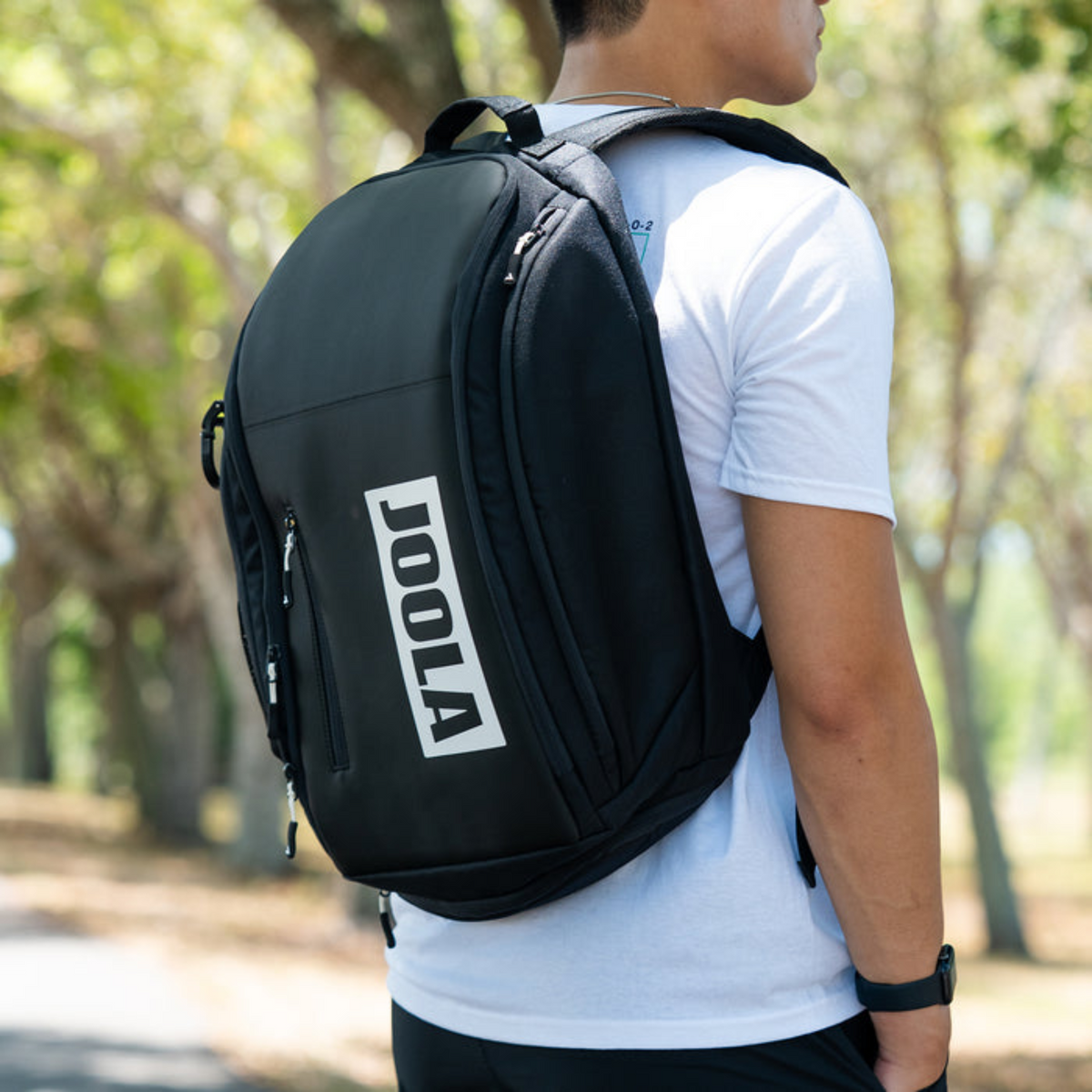 Person wearing a black backpack with 'JOOLA' branding outdoors.