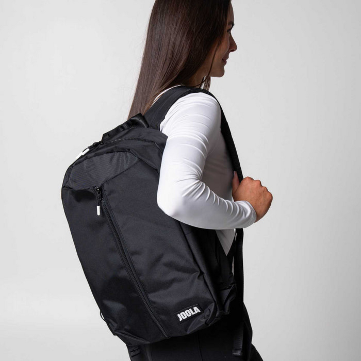 Person wearing a black backpack with a plain background