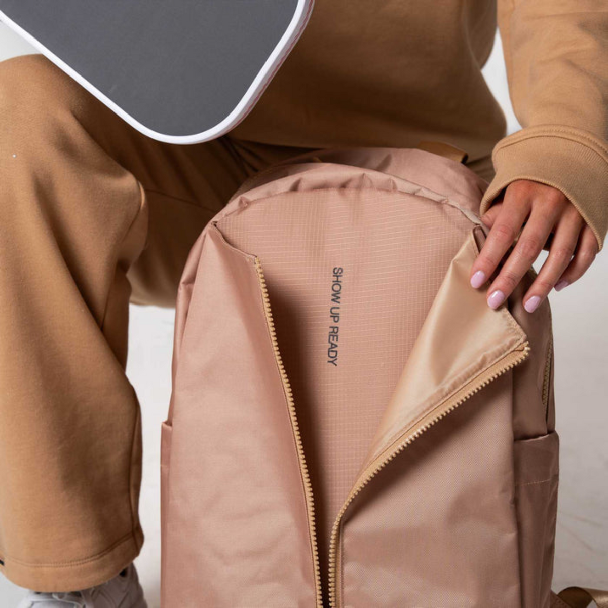 Person wearing a beige jacket with a visible brand logo on a plain background