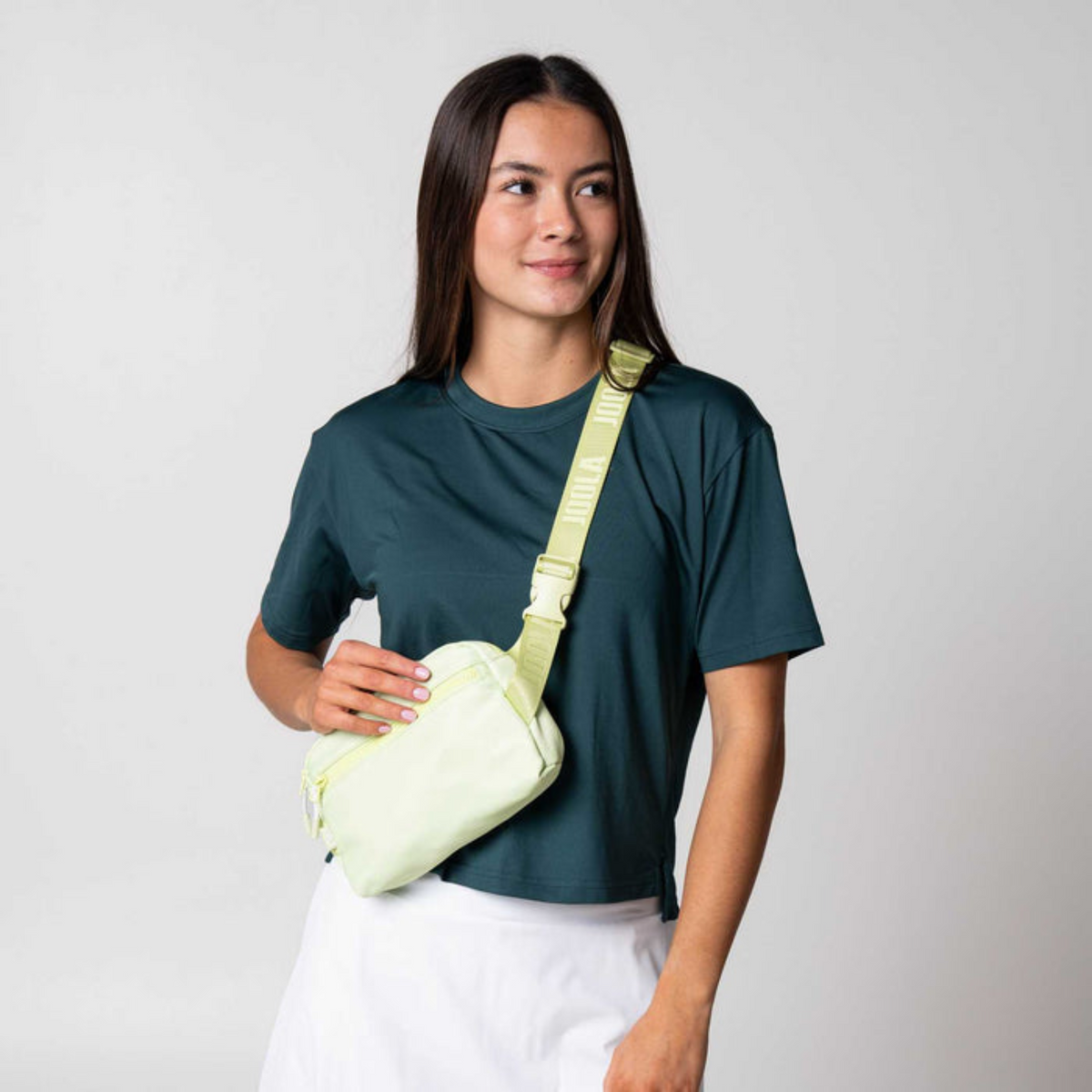 Woman wearing a light green crossbody bag against a plain background