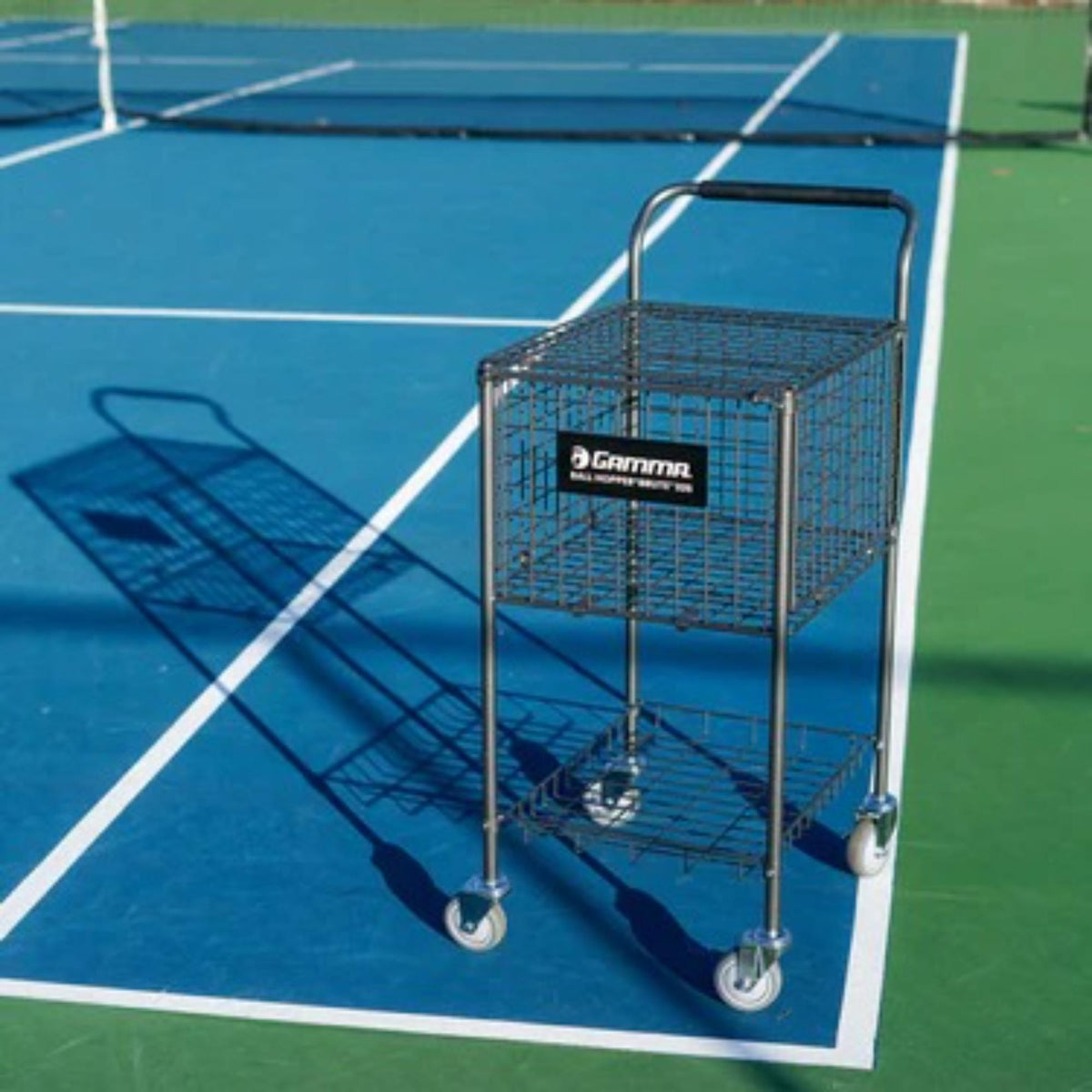 Ball hopper cart with a large wire basket, lower storage shelf, handle for transport, and four caster wheels for easy mobility.
