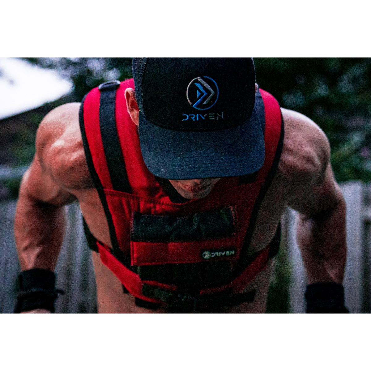 Person wearing a red weight vest and black cap with 'DriVen' branding outdoors.