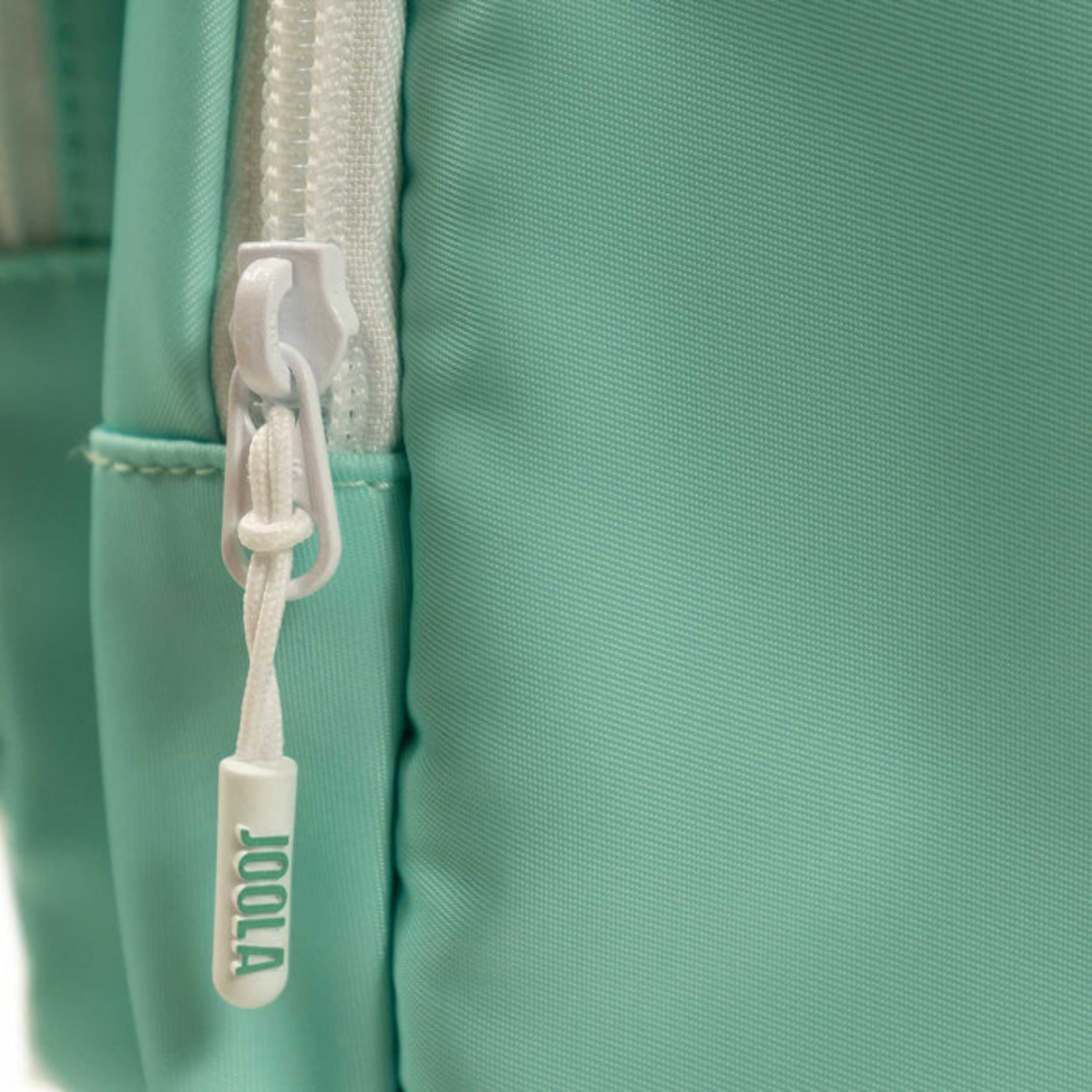 Close-up of a teal bag with a white zipper pull featuring the brand 'Joola'.