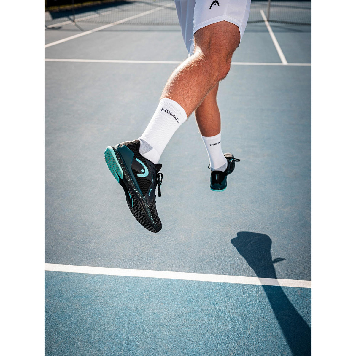 Tennis player jumping on a hard court wearing black and teal HEAD Sprint Pro 4.0 SF tennis shoes, with focus on the outsole traction, midsole cushioning, and dynamic on-court movement.
