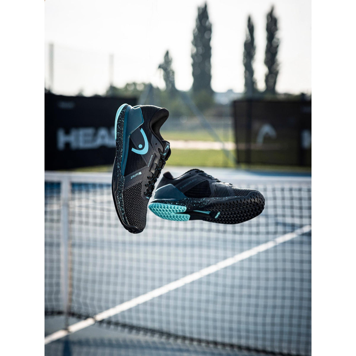 Two HEAD Sprint Pro 4.0 SF tennis shoes captured mid-air above a hard-court net, highlighting the lightweight construction, breathable mesh upper, and teal-accented outsole designed for speed, stability, and explosive movement on court.