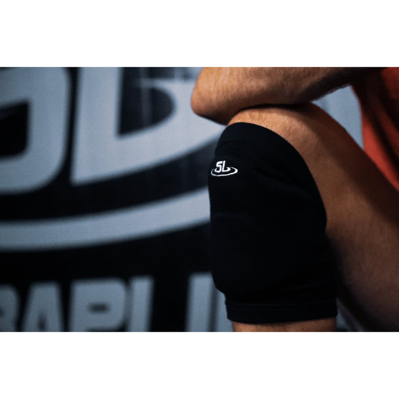 Black wrist wrap with a logo on a person's wrist, blurred background with visible brand name.