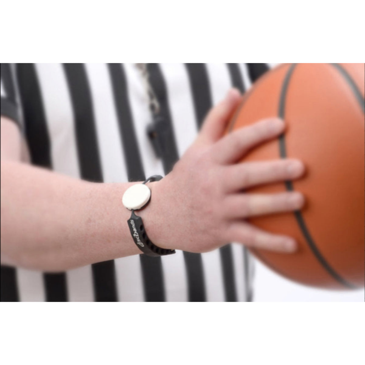 Hand holding a basketball with a blurred black and white striped background