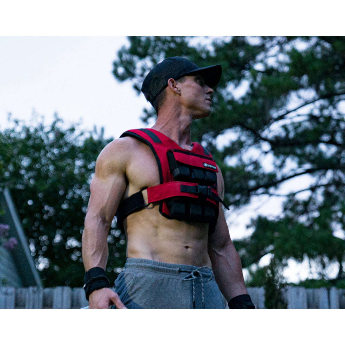 Man wearing a red weight vest outdoors with trees in the background