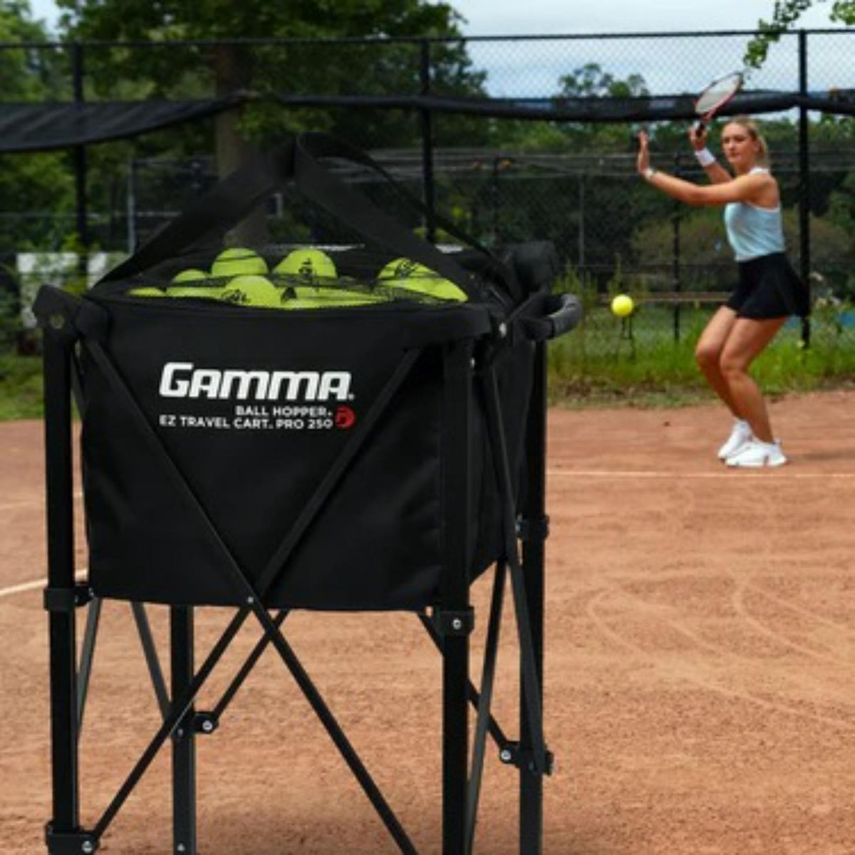 Portable ball hopper cart with rolling wheels, collapsible frame, and attached storage basket for transporting sports balls.