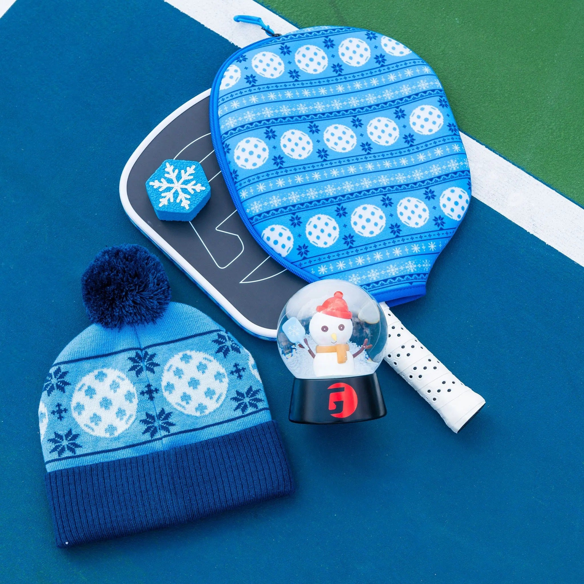 Pickleball gift bundle featuring paddles, paddle cover, winter hat, novelty dampener, and decorative snow globe accessory.