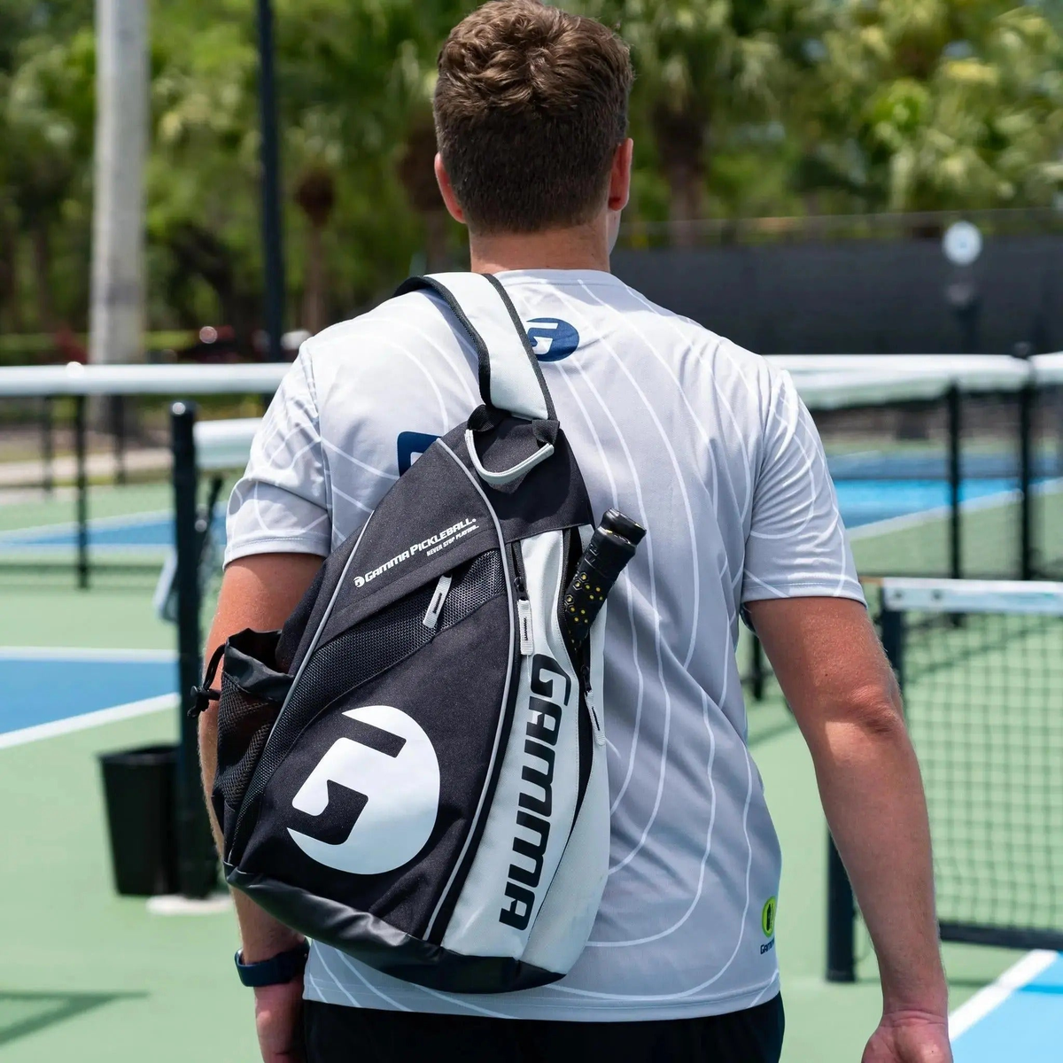 Pickleball sling bag with multiple compartments, mesh pocket, and side holder for carrying paddles, balls, and accessories.