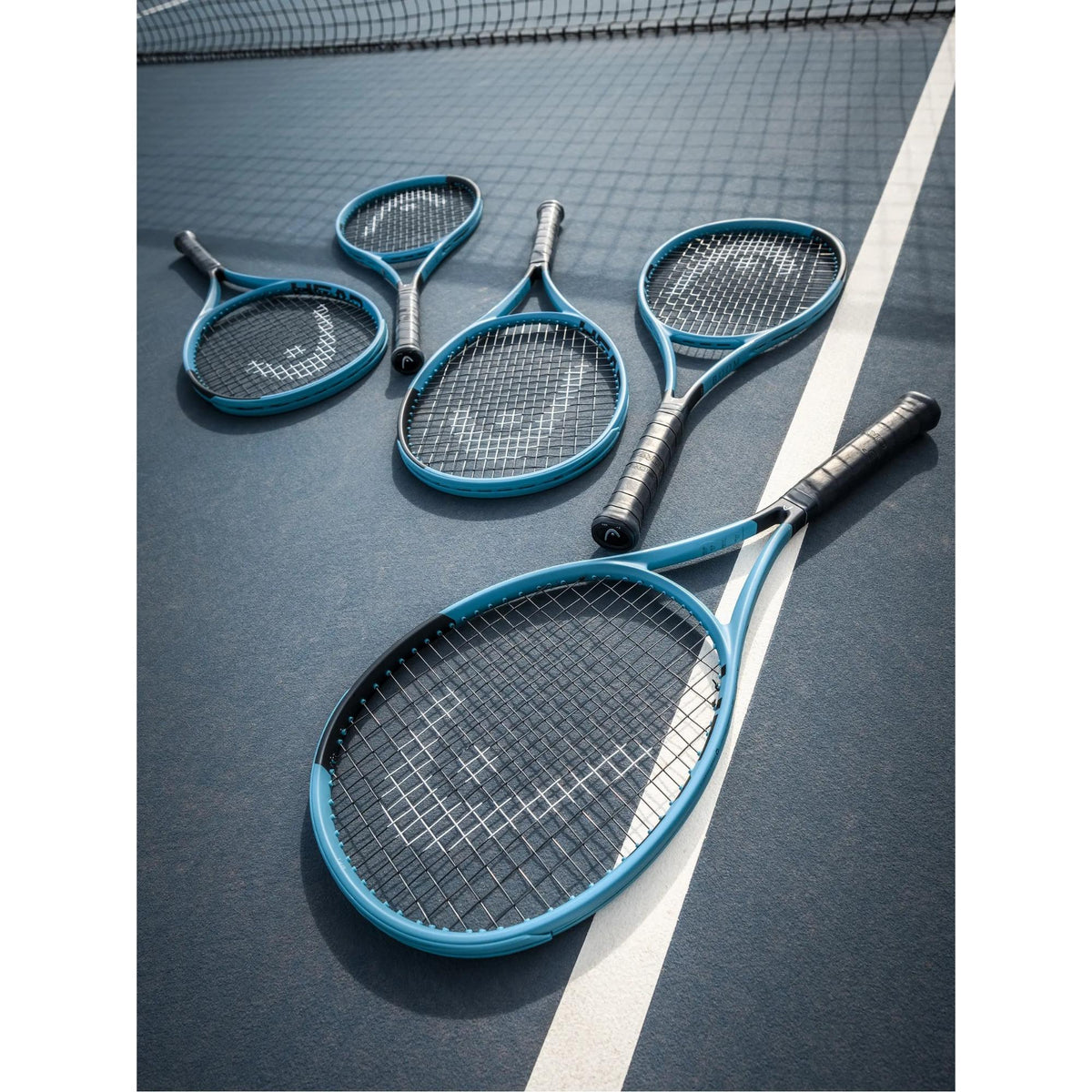 Multiple HEAD Boom TEAM teal tennis racquets arranged on an outdoor tennis court near the net.