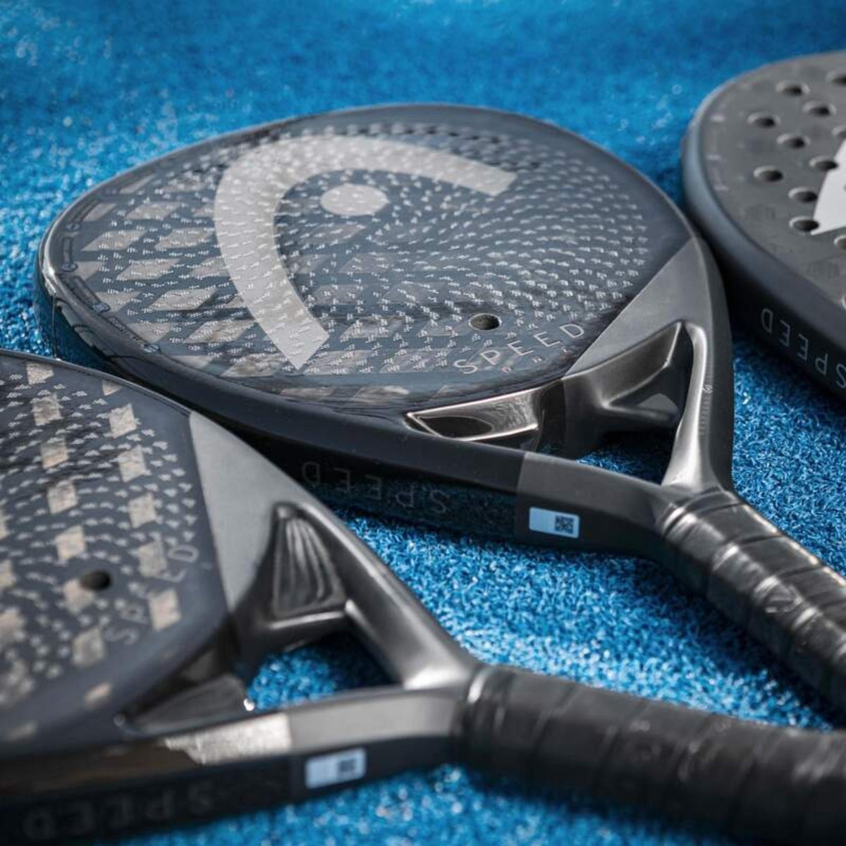 Close-up of HEAD Speed One padel racket lying on blue court surface highlighting carbon fiber detail.