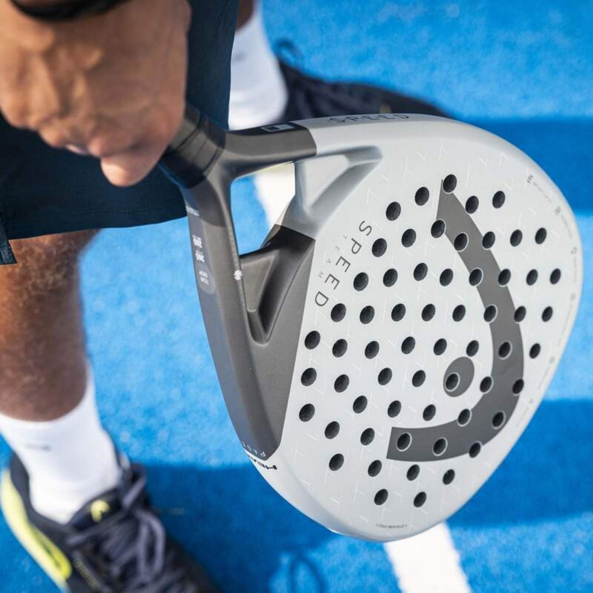 Player gripping a grey HEAD Speed Team padel racket on a blue padel court, close-up action shot.