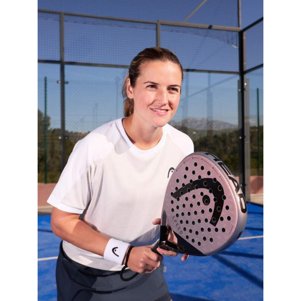 Female padel player holding a rose Head Speed racket on an outdoor blue court.